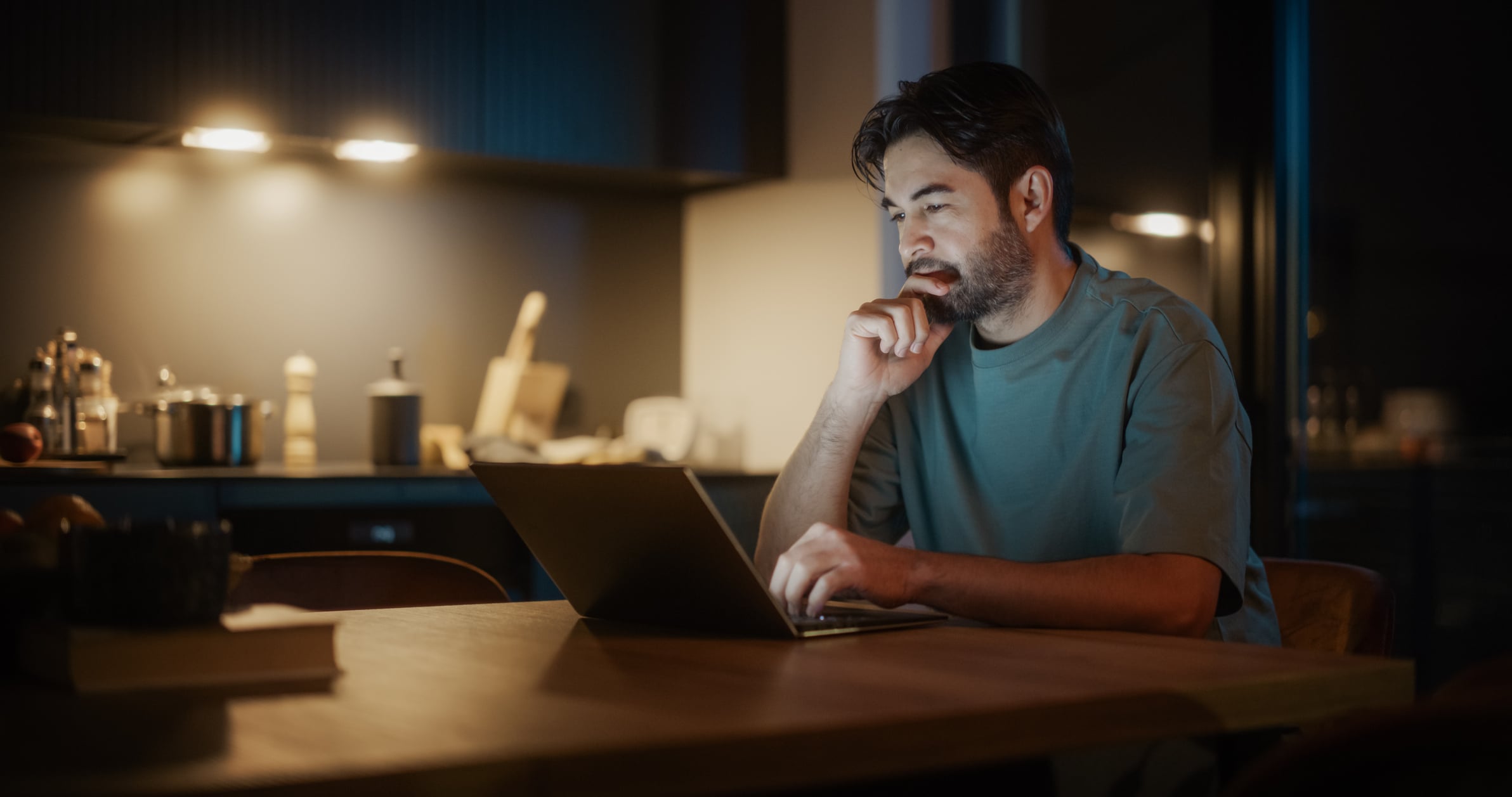 Man Sitting at a Table in a Kitchen and Using Laptop Computer